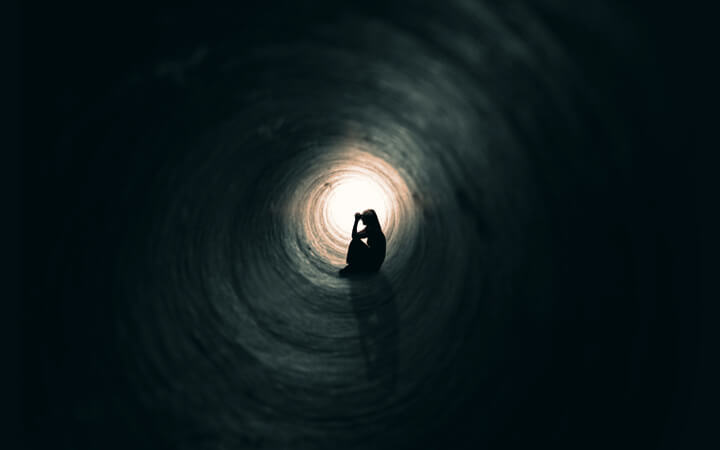 The silhouette of a praying woman sitting in a dark tunnel with a light at the end.