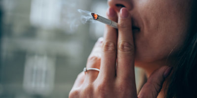 Unerkennbare junge Frau raucht am Fenster eine Zigarette