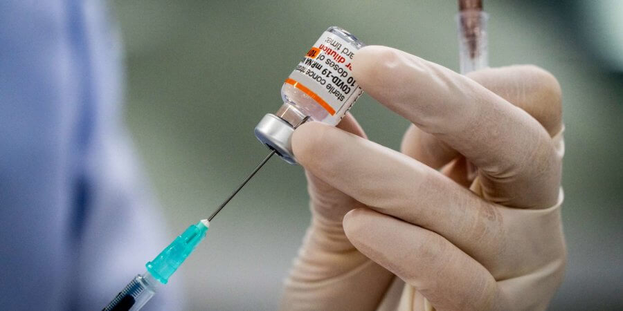 Pfizer-BioNTech COVID-19-Impfstoffdosen (Comirnaty), die von behandschuhten Medizinern mit Spritze zubereitet werden