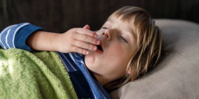 Kleiner kranker Junge hustet, während er zu Hause einen Virus im Bett hat.