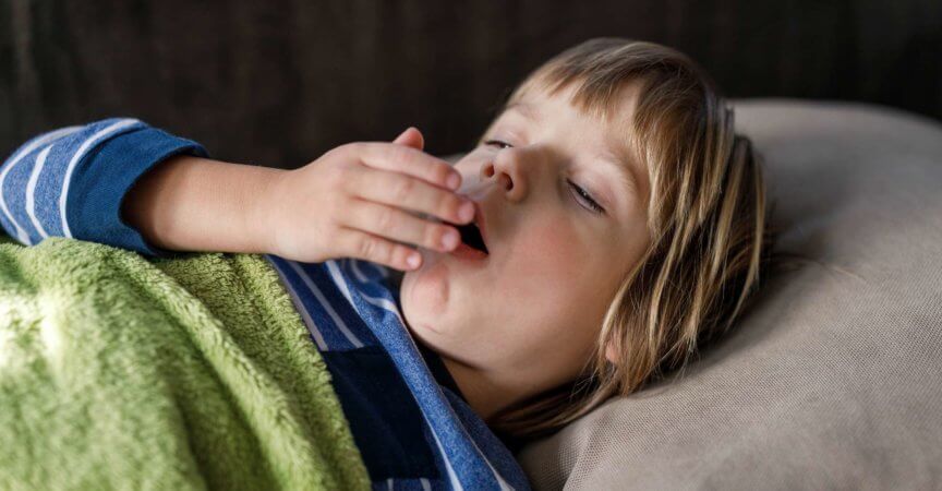 Kleiner kranker Junge hustet, während er zu Hause einen Virus im Bett hat.