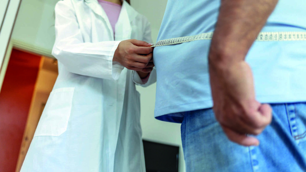 Ein Ernährungsarzt misst den Körper eines männlichen Patienten mit einem Maßband auf Fettgewebe und Übergewicht.