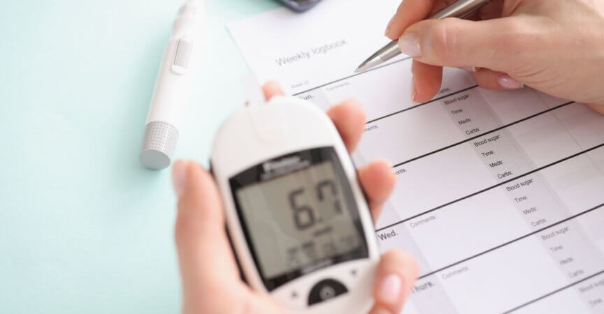 Glucometer with blood test results in patient hand fills in results in daily report. Diabetes mellitus concept