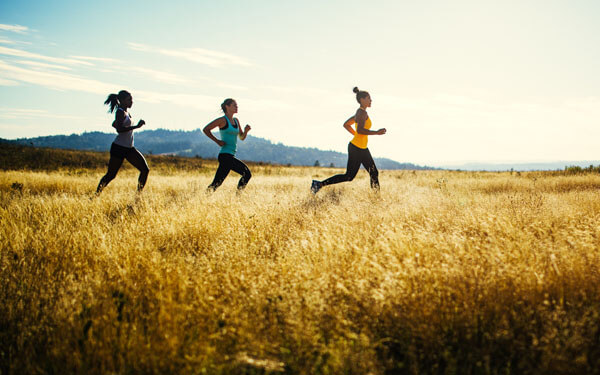 Eine Gruppe von jungen Frauen joggen bei Sonnenaufgang über ein Feld