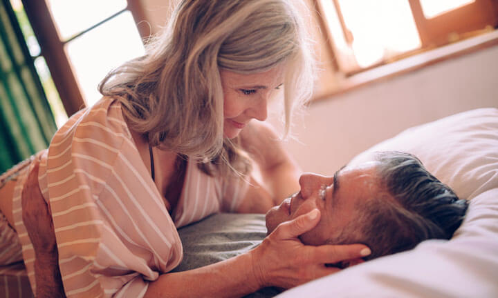 Seniorenpaar flirtet und schaut sich lustvoll in die Augen, während es sich im Bett entspannt