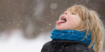 Süßer blonder Junge, der Schneeflocken mit seiner Zunge fängt, während er in einem Winterpark spazieren geht. Kind hat Spaß mit Schnee im Freien.