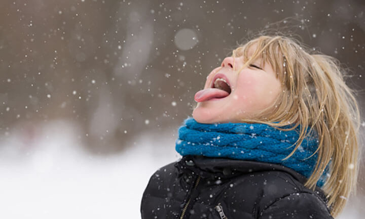 Süßer blonder Junge, der Schneeflocken mit seiner Zunge fängt, während er in einem Winterpark spazieren geht. Kind hat Spaß mit Schnee im Freien.
