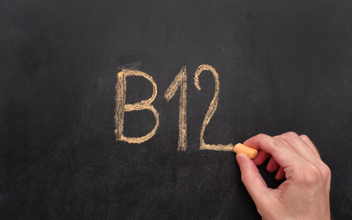 Mann schreibt Wort B12 auf Tafel. Vitamin B12-Konzept. Nahaufnahme.