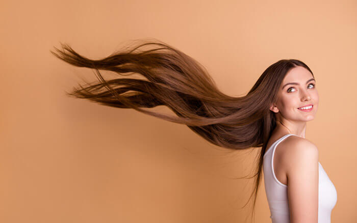 Portait einer jungen Frau deren lange Haare hinter ihr in der Luft schweben vor pastellbeigem Hintergrund