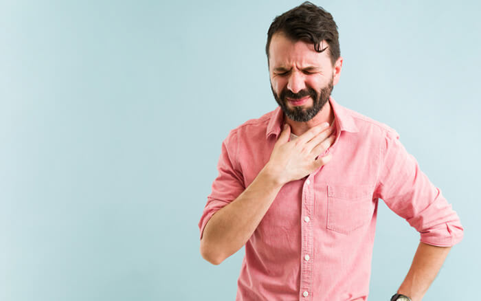 Leiden unter Halsschmerzen isoliert vor einem Hintergrund. Lateinischer Mann mit Reflux aufgrund einer schweren Mahlzeit oder eines Abendessens
