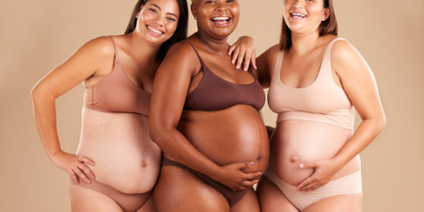 Portraitfoto mit drei lachenden, schwangeren Frauen in Unterwäsche