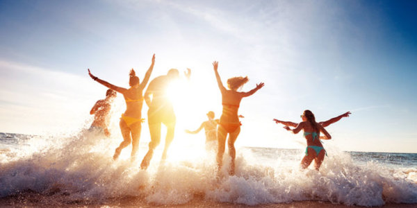 Eine große Gruppe von sieben glücklichen Freunden hat Spaß und läuft am Strand bei Sonnenuntergang, um Sonnenlicht und Wellen zu genießen