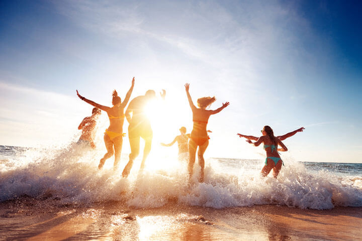 Eine große Gruppe von sieben glücklichen Freunden hat Spaß und läuft am Strand bei Sonnenuntergang, um Sonnenlicht und Wellen zu genießen