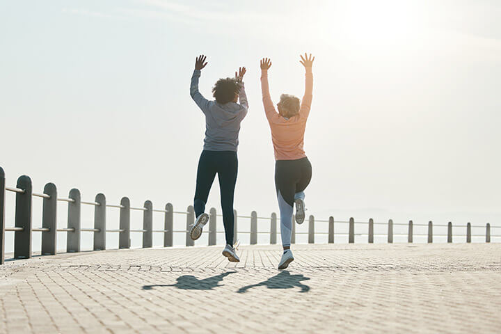Zwei Frauen in Fitnesskleidung am Strand machen einen Energiesprung.