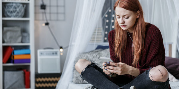Teenager sitzt auf ihrem Bett und schaut auf das Smartphone.