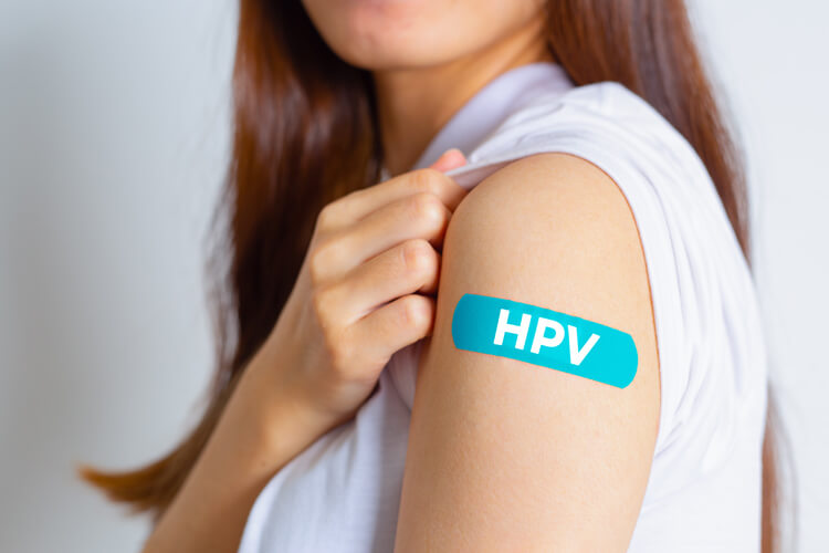 Junge Frau zeigt ihren Oberarm auf dem ein Pflaster mit der Aufschrift HPV klebt.