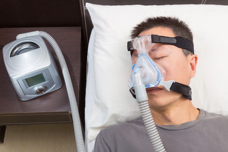 Mann mittleren Alters liegt im Bett mit Maske und Gerät gegen Schlafapnoe.