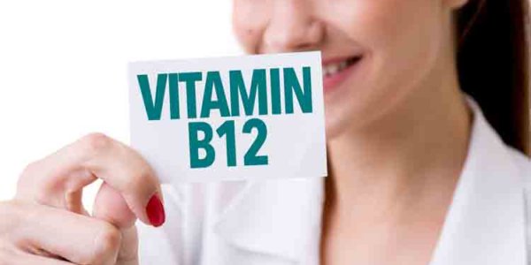 Frau hält ein Schildchen mit der Beschriftung Vitamin B12 in die Kamera