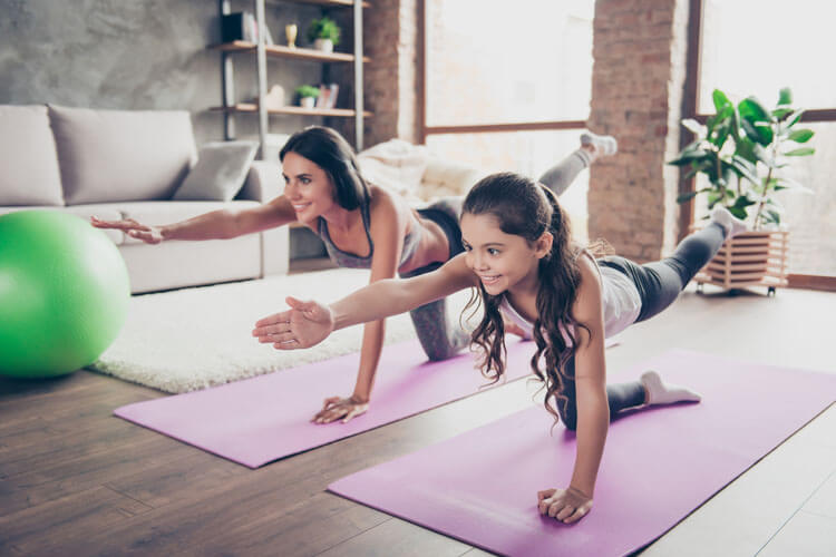 Mutter und Tochter machen im Wohnzimmer Yoga