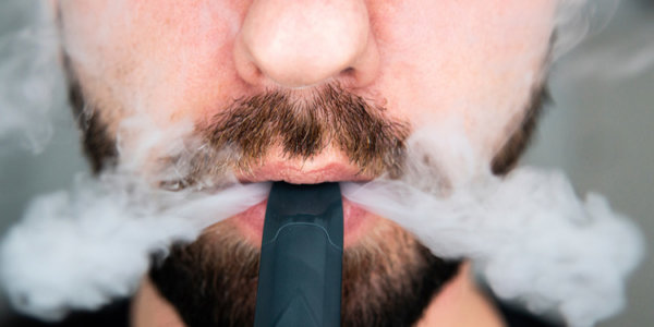 Nahaufnahme der unteren Gesichtshälfte eines Mannes, der eine E-Zigarette raucht.