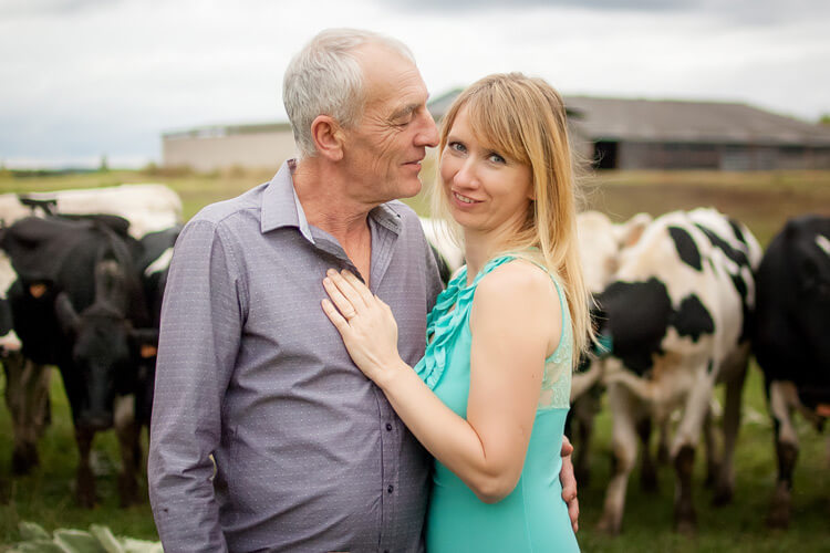 Älterer Mann umarmt seine jüngere blonde Frau auf einer Kuhwiese.