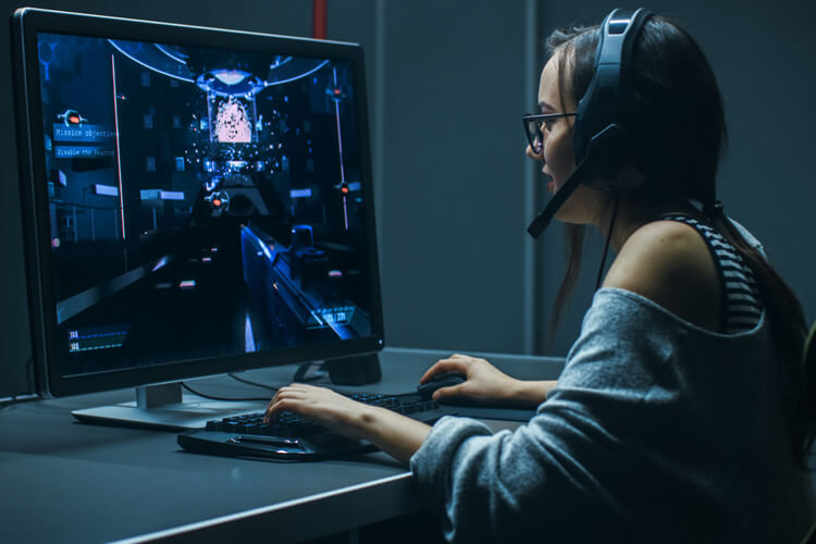 Junge Frau spielt an einem PC einen Ego-Shooter.
