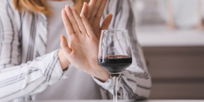 Frau verwirft die Hände vor einem Glas Wein. Alkoholverzicht.
