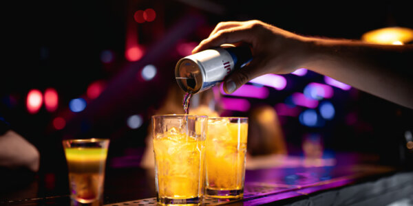 Hand leert einen Energy Drink in ein Glas auf einer Bar während einer Party.