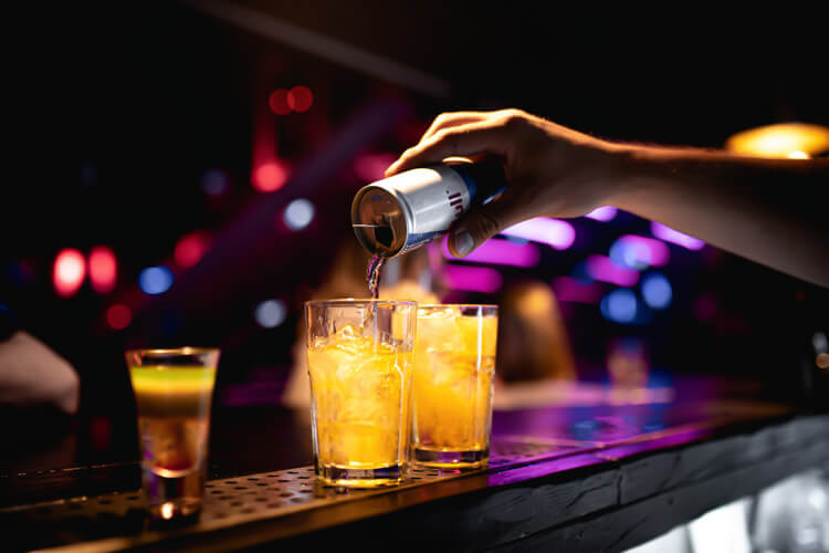 Hand leert einen Energy Drink in ein Glas auf einer Bar während einer Party.