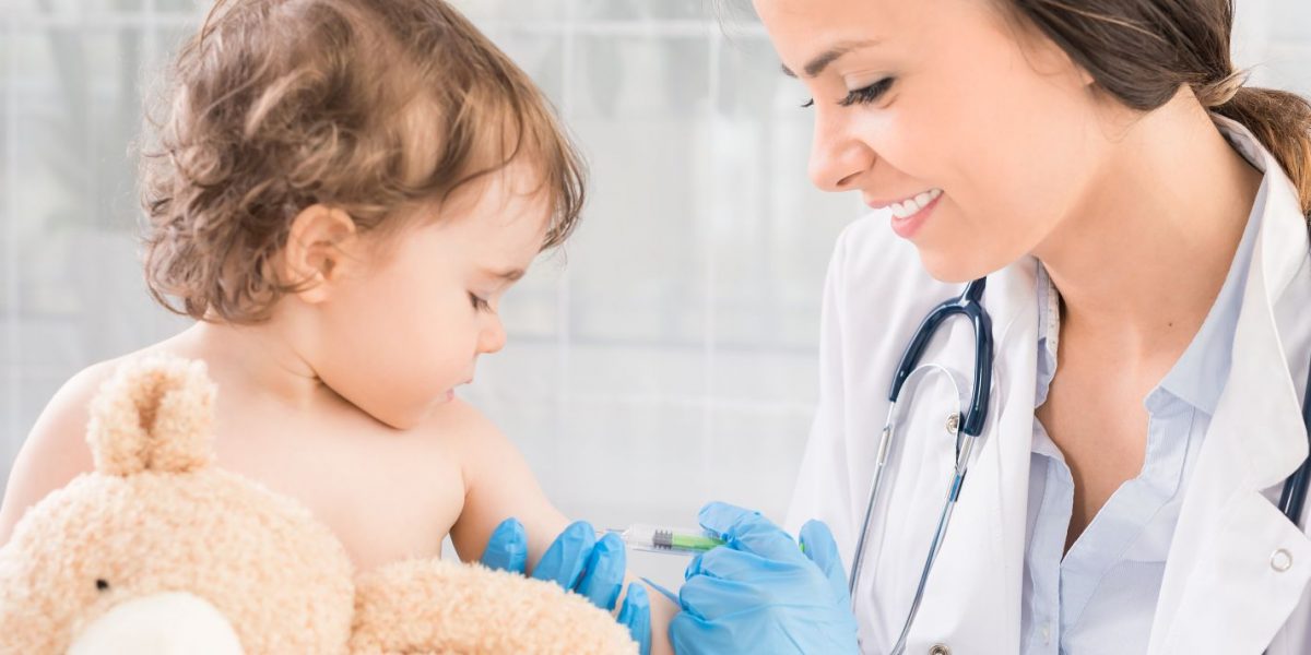 Young woman pediatrician performs a vaccination of a little girl. The girl is holding a mascot.